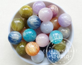 May include: A white bowl filled with colorful, swirled, round plastic beads. The beads are in shades of blue, green, pink, and yellow.