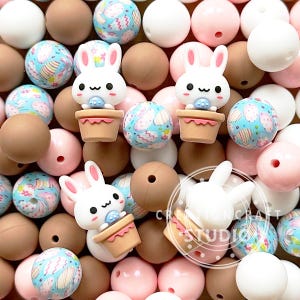 May include: A collection of colorful silicone beads featuring a bunny rabbit holding an Easter egg in a pot. The beads are in shades of brown, pink, white, and blue with a patterned design.