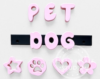 May include: A set of light pink plastic letters spelling PET DOG, with the word DOG mounted on a black horizontal bar. Below are four light pink shapes: a five-pointed star, a paw print, a heart, and a five-petaled flower, all with cutouts.