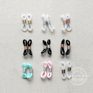 May include: Nine pairs of clear, black, pink, and light blue eyeglass holders with metal accents. The holders are arranged in three rows of three.