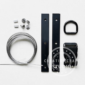 Può includere: Un assortimento di componenti hardware neri, tra cui due piastre rettangolari, un anello a D e una fibbia. Include anche una bobina di filo d'argento, viti e rivetti. Il testo "CREATION CRAFT STUDIO" è visibile.