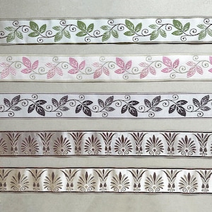 Könnte beinhalten: Fünf verschiedene Bänder aus Stoff mit verschiedenen floralen und geometrischen Mustern. Die Bänder sind weiß mit grünen, rosa, schwarzen, braunen und goldenen Akzenten.