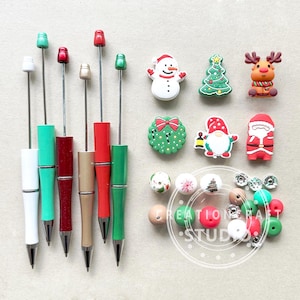 以下が含まれることがあります： ペン、ビーズ、チャームを含むクリスマスをテーマにしたクラフト用品のセット。チャームには、雪だるま、クリスマスツリー、トナカイ、リース、ノーム、サンタクロースが含まれています。ビーズは赤、緑、白、茶色です。ペンは白、緑、赤、金です。