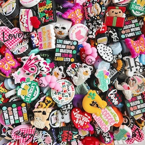 May include: A collection of colorful,  decorative shoe charms with various designs and phrases, including "Live Simple", "Dream Big", "Be Grateful", "Give Love", "Laugh Lots", "St. Patrick's Day", "Coffee Things", "Just You & Me", and "Cat Mom".