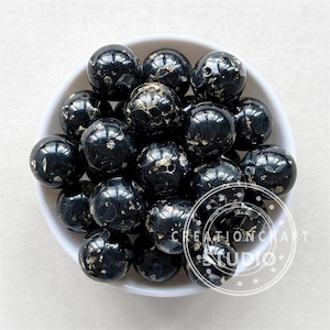 May include: A bowl of black and gold silicone beads. The beads are round and have a speckled appearance. The beads are ideal for making jewellery or other crafts.
