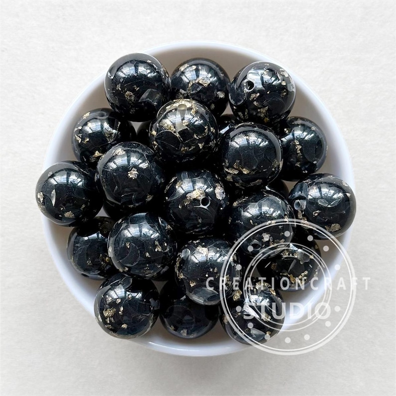 May include: A bowl of black and gold silicone beads. The beads are round and have a speckled appearance. The beads are ideal for making jewellery or other crafts.