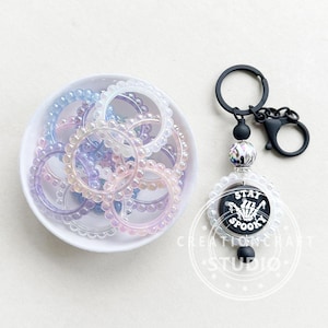 May include: A set of iridescent clear plastic rings with a black and white charm with the text "Stay Spooky" on a black background. The charm is attached to a black key chain.