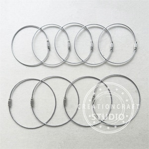 May include: Ten silver key rings with a cable construction. The rings are arranged in two rows of five.