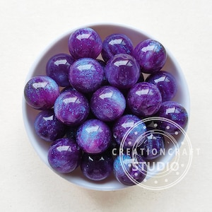 May include: A bowl filled with purple and blue iridescent resin beads. The beads have a galaxy-like appearance with swirls of colour and glitter.
