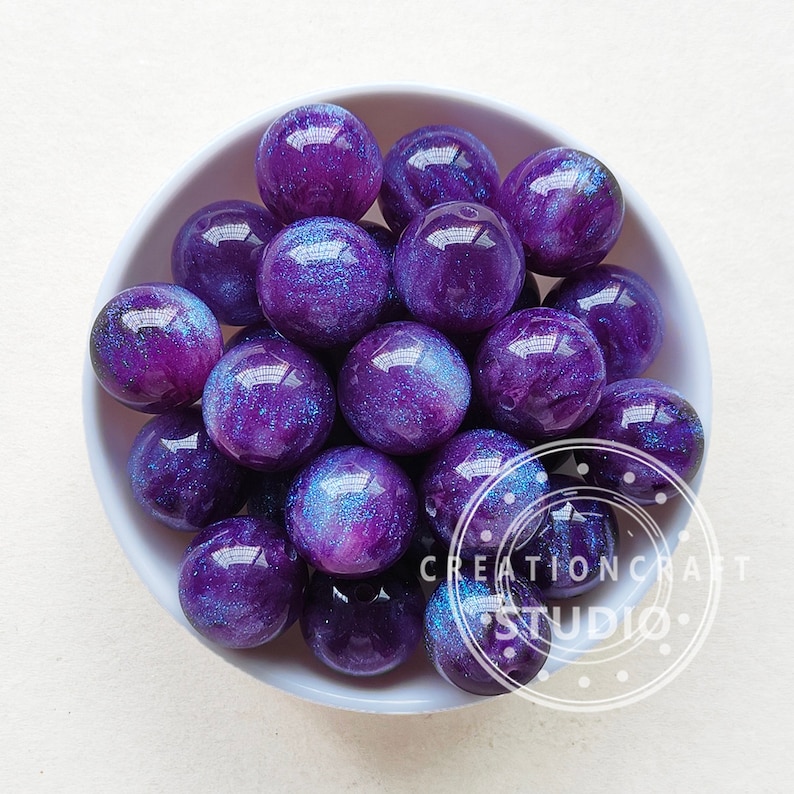 May include: A bowl filled with purple and blue iridescent resin beads. The beads have a galaxy-like appearance with swirls of colour and glitter.