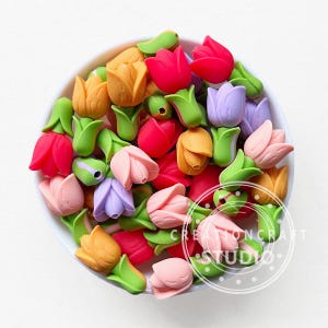 May include: A bowl filled with colorful tulip-shaped embellishments. The tulips are in shades of red, pink, yellow, and purple, with green leaves. The embellishments are likely for crafts or decorations.