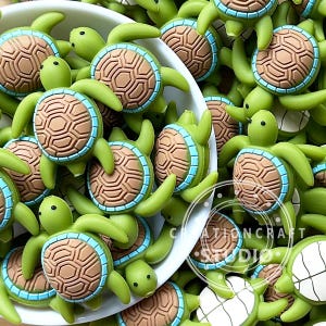 Puede incluir: Una colección de adornos verdes con forma de tortuga, con detalles de caparazón marrón y ribete azul claro. Las tortugas están esparcidas alrededor de un cuenco blanco, algunas se desbordan. La imagen es brillante, mostrando los detalles.