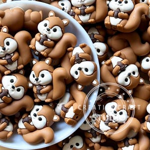 Puede incluir: Una colección de pequeñas cuentas tridimensionales con forma de ardilla en tonos marrón y blanco. Cada ardilla aparece sosteniendo una pequeña bellota marrón. Las cuentas son lisas y presentan un diseño de dibujos animados.