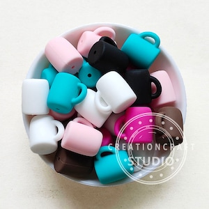May include: A bowl filled with colorful silicone mug shaped beads. The beads are in various colors including pink, white, brown, black, and turquoise.