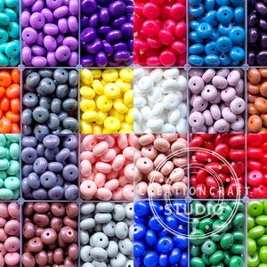 May include: Assortment of 12 colors of round, flat, plastic beads. Each color is displayed in a separate square compartment. The beads are all the same size and shape.