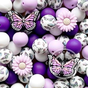 Pode incluir: Uma coleção de contas de silicone roxas, brancas e lavanda com designs de borboletas e flores. As contas são perfeitas para fazer colares, pulseiras ou outras joias.