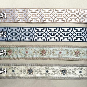 May include: Four samples of decorative trim with different patterns. The first trim is white with a gold geometric pattern. The second trim is white with a black geometric pattern. The third trim is light blue with a floral pattern. The fourth trim is cream with a floral pattern.
