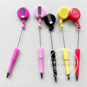 May include: Five retractable pens with different colored tops and retractable cords. The pens are pink, pink, black, yellow, and red.