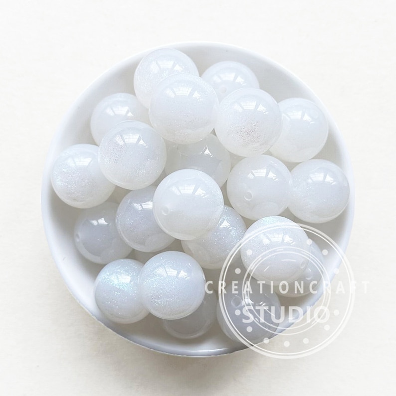 May include: A bowl of white, iridescent, round, plastic beads. The beads have a subtle sparkle.