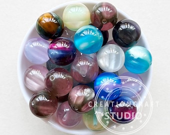 May include: A bowl filled with iridescent glass beads in various colors, including purple, blue, pink, and green. The beads have a shimmering, opalescent finish.