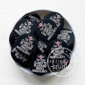 Peut inclure: Un bol rempli de boutons ronds noirs avec un motif floral blanc et le texte "Je suis trop maladroit pour être autour de la masculinité fragile".