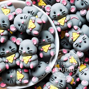 Puede incluir: Primer plano de numerosos adornos grises con forma de ratón, cada uno sosteniendo un trozo de queso amarillo. Los ratones tienen orejas, pies y narices rosas, con ojos y bigotes negros. Están dispuestos en un cuenco blanco.