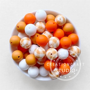 May include: A bowl filled with orange, white and tan silicone beads. The beads have different patterns, including plaid and swirls.