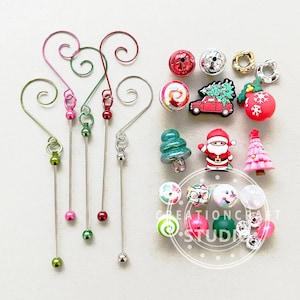 May include: A set of five silver wire ornament hangers with green, pink, and silver beads. The set also includes a variety of Christmas-themed beads, including a red car with a Christmas tree on top, a Santa Claus, a snowman, and a Christmas tree.