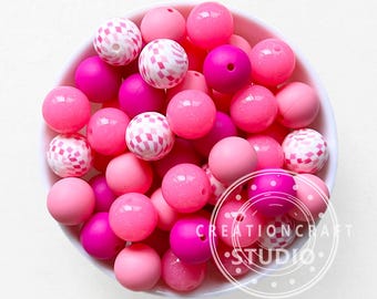May include: A white bowl filled with various shades of pink beads. The beads are round and smooth, with some featuring a white and pink checkered pattern. The image includes the text "CREATIONCRAFT STUDIO".