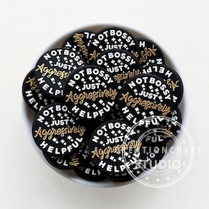 May include: A bowl filled with black and white round stickers that say "Not Bossy, Just Aggressively Helpful" in gold lettering.