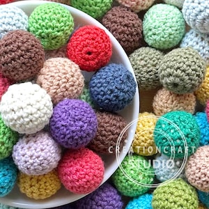 May include: A bowl filled with colorful crocheted balls. The balls are made of yarn in various colors, including pink, purple, green, blue, brown, and yellow.