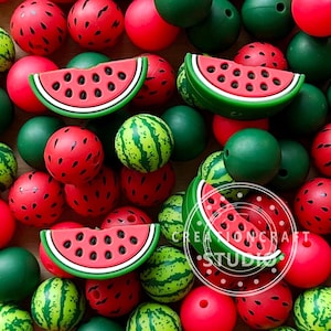 Könnte beinhalten: Eine Sammlung roter, grüner und gelber Perlen und Anhänger zum Thema Wassermelone. Die Perlen sind rund und haben ein Wassermelonen-Schalendesign. Wassermelonenscheiben-Anhänger sind ebenfalls vorhanden, mit schwarzen Samendetails.