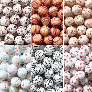 Pode incluir: Uma coleção de contas redondas em vários designs e cores. Algumas contas apresentam padrões florais em branco e castanho. Outras têm padrões listrados em laranja e vermelho. Contas adicionais têm uma base branca com pontos vermelhos ou padrões em preto e branco.