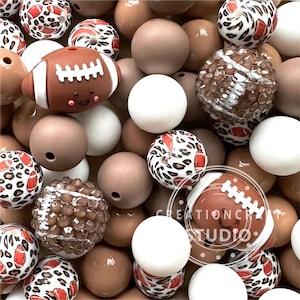 May include: A collection of brown, white, and leopard print silicone beads with football and football-themed designs. The beads are perfect for making necklaces, bracelets, or other crafts.