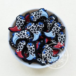 May include: A bowl filled with cow print cowboy boot charms. The charms are made of silicone and have blue and red accents.