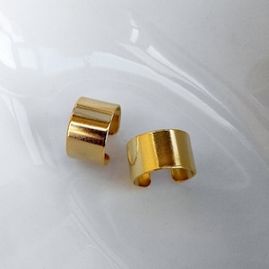 Könnte beinhalten: Zwei goldfarbene Ohrringe, die jeweils ein einfaches, abgerundetes und leicht gebogenes Design haben. Die Ohrringe sind aus Metall und haben eine glatte, polierte Oberfläche.