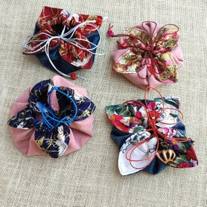 May include: Four fabric pouches with different floral patterns. The pouches are made of a soft, pink fabric with a blue and white floral print. The pouches are tied with a string and have a drawstring closure.