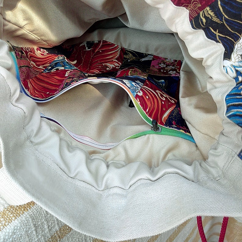 May include: A white canvas drawstring bag with a zippered pocket. The pocket is lined with colourful fabric featuring a Japanese-inspired pattern of fish and waves.