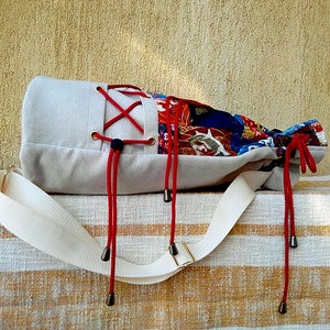 May include: A beige canvas bag with red and black straps and a colourful patterned fabric lining. The bag is sitting on a striped fabric surface.