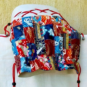 May include: A red and white drawstring bag with a patchwork design featuring various colours and patterns, including blue, green, and gold. The bag is made of fabric and has a unique, handmade look.