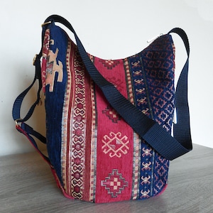 May include: A blue and red patterned tote bag with a long adjustable strap. The bag has a geometric design with a variety of colors and patterns.
