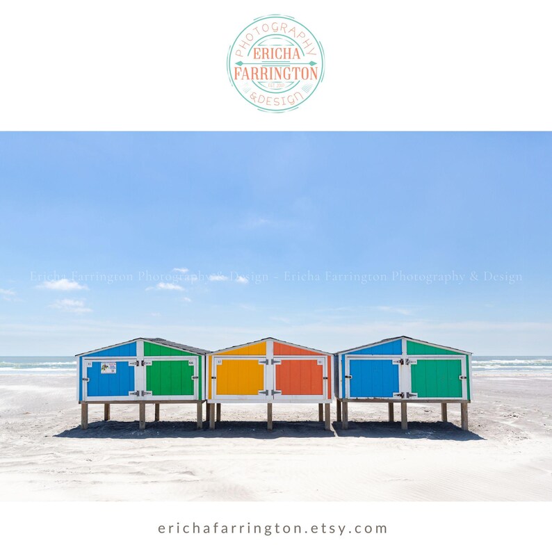 May include: A scenic beach photograph featuring three colorful beach huts. The huts are painted in vibrant hues of blue, green, yellow, and orange, with white doors and trim. The image is set against a backdrop of a clear blue sky and the ocean.