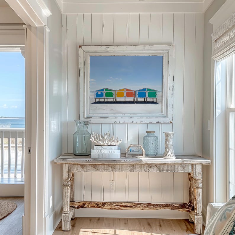 May include: A rustic wooden console table with decorative items, including a framed beach scene with colorful beach huts. The table has a distressed finish and is adorned with vases, coral, and books, creating a coastal theme.
