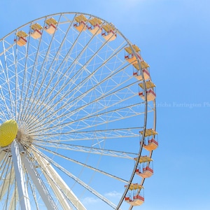 May include: A large Ferris wheel against a bright blue sky. The wheel's frame is white, with yellow and red passenger cabins. The central hub is yellow, and the spokes create a geometric pattern. A sunny day at an amusement park.