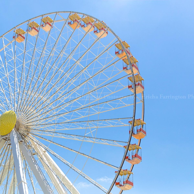 May include: A large Ferris wheel against a bright blue sky. The wheel's frame is white, with yellow and red passenger cabins. The central hub is yellow, and the spokes create a geometric pattern. A sunny day at an amusement park.