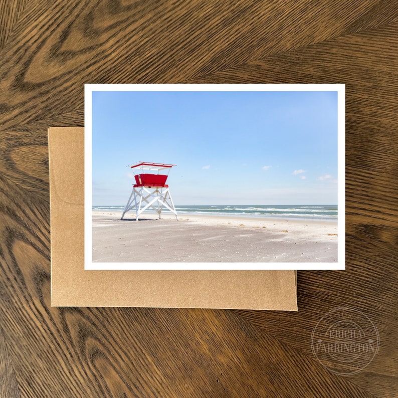 Puede incluir: Un puesto de salvavidas rojo y blanco en una playa de arena con cielo azul y olas del oc&eacute;ano en el fondo.