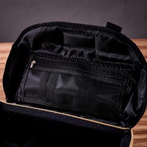 May include: A tan canvas travel bag with a black zippered interior. The bag has multiple compartments and a mesh pocket.