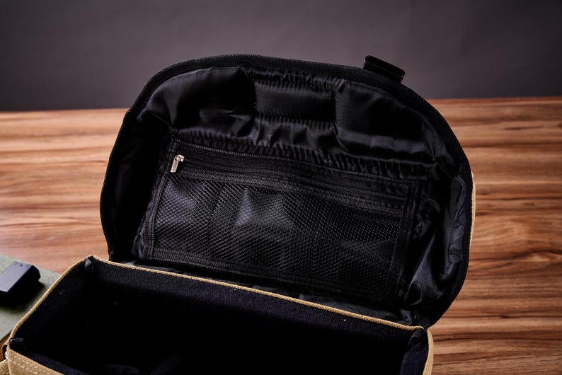 May include: A tan canvas travel bag with a black zippered interior. The bag has multiple compartments and a mesh pocket.