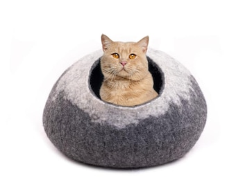 May include: A gray and white felt cat bed with a cat inside. The cat is looking directly at the camera.