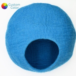 Könnte beinhalten: Ein blaues Katzenbett aus Filz in Form einer Kuppel mit einer runden Öffnung. Das Bett ist aus weichem, natürlichem Wollfilz.